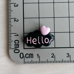 Vue macro de l'accessoire en résine nuage noir avec texte Hello rose sur tapis