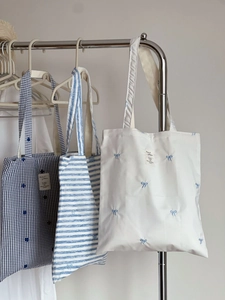 Detailed view of striped and bow-embroidered cotton canvas tote bags hanging on a rack