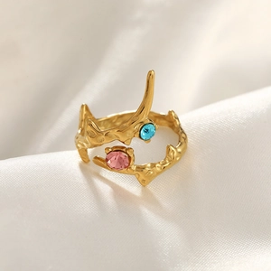 Detail view of a hammered gold open ring featuring textured vines with blue and pink gems