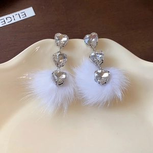 Detailed view of silver heart earrings with sparkling rhinestones and white fur pom-poms