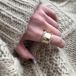 Close-up of wide gold-plated geometric ring worn on hand with cozy sweater background