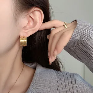 Detailed close-up of gold hoop earrings with multi-line textured finish on a model