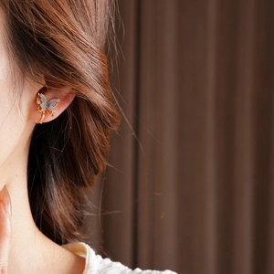 Close-up of a 18k gold butterfly ear cuff with light blue wings and sparkling zircons