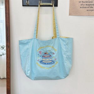 Detail of blue canvas tote bag featuring cake embroidery and plaid handle straps