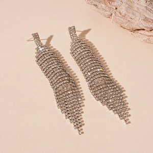 Vue détaillée de longues boucles d'oreilles à franges argentées et strass sur décor de pierre