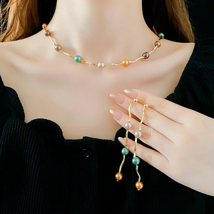 Detail of wavy gold necklace and tassel earrings with colorful pearl-like beads