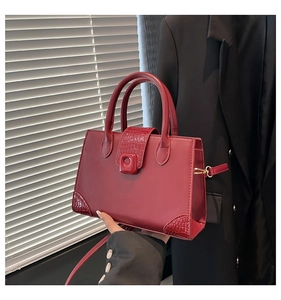 Detail showing the burgundy faux crocodile texture and square lock on the handbag