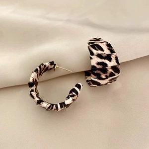Detailed view of C-shaped leopard print fabric earrings on soft white fabric background