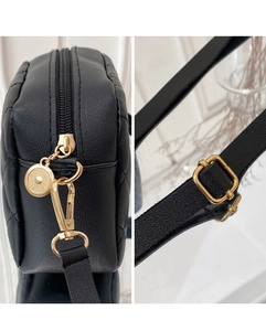 Detail of black quilted leather bag featuring gold zipper and adjustable metal strap buckle