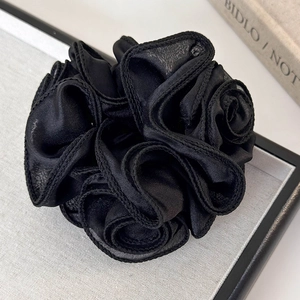 Close-up of black satin rose scrunchie with layered fabric texture on a grey tray