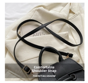 Close-up of black lychee leather handbag with golden buckles on a white blazer