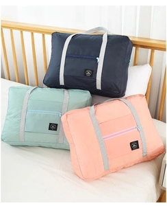 Three colorful large travel storage bags in navy, mint, and pink on a white bed