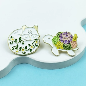 Macro detail of cute enamel pins featuring a white fox and succulent shell turtle badge
