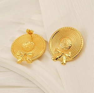 Détail des boucles d'oreilles nœud dorées avec forme de chapeau et texture tissée