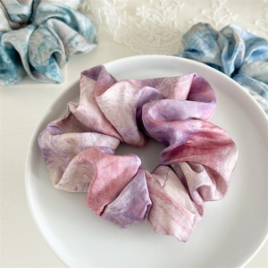 Detailed view of pink tie-dye satin scrunchie placed on a white ceramic plate