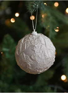 Detailed view of beige jacquard fabric Christmas ball hanging on a green tree branch