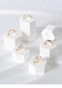 Detail of five gold rings with pearls and rhinestones on white geometric stands