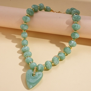 Detail of green marbled acrylic heart pendant and gold beads on a sweater chain