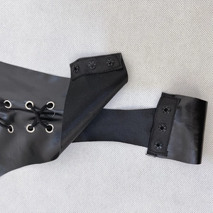 Detailed view of metal eyelets with lacing and snap button closures on black PU jumpsuit