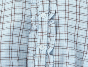 Detailed close-up of light blue plaid dress with ruffled trim and round buttons