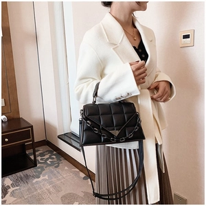 Fashionable black quilted handbag with chunky metal chain and leather strap on model