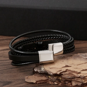 Men's hand-woven black leather bracelet with silver metal clasp on rustic wooden background