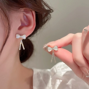 Détail de la boucle d'oreille nœud doré avec pierre œil de chat et pompons en strass