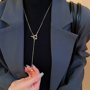 Detail of gold OT buckle necklace with snake chain and polished bead on black sweater