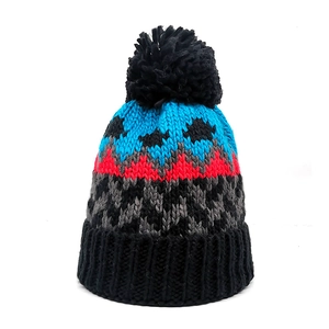 Close-up of thick knit beanie with colorful geometric patterns and a black faux fur pompom