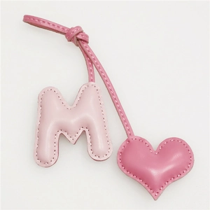 Detail showing hand-stitched leather letter M and heart charm for bags and keychains