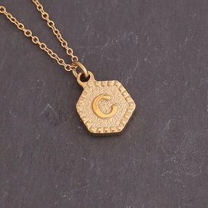 Detailed macro view of a hexagonal gold pendant with embossed letter C and hammer texture