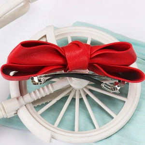 Close-up of red faux leather bow hair clip with metal fastener on decorative background