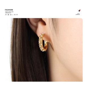 Gros plan de boucles d'oreilles créoles dorées 18K avec perles et cristaux sur un mannequin