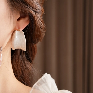 Close-up of irregular off-white marble texture hoop earring worn by a model