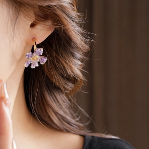 Close-up of a model wearing a purple flower C-shaped earring with gold accents and crystals