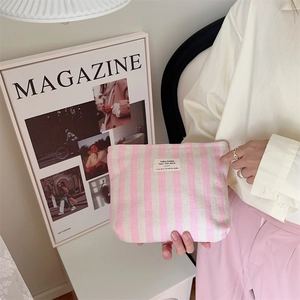 Macro view of pink striped fabric makeup bag with textile label held by a model