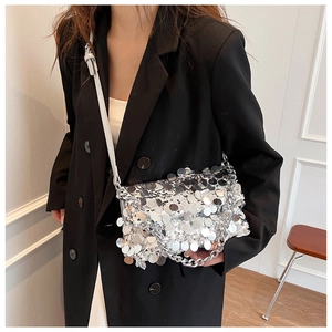 Detail of silver sequin handbag with metallic chain strap worn by a model in a suit