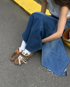 Close-up of distressed denim skirt hem with frayed edges and brown suede sneakers