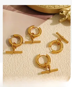Détail de boucles d'oreilles créoles dorées avec pendentifs barre en T sur fond minimaliste