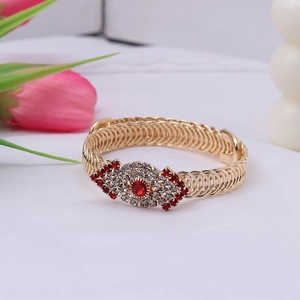Detail of a vintage golden spiral woven bracelet featuring a red rhinestone devil eye