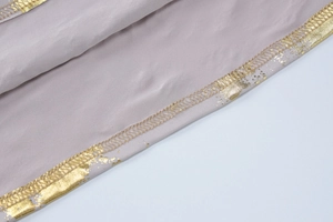 Detail of light mauve fabric featuring gold bronzing trim and precise stitching work