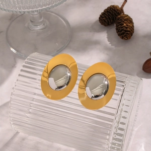 Macro detail of geometric gold and silver elliptical earrings on a textured glass surface