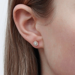 Close-up of rose gold flower stud earrings with shimmering zircon petals on a model