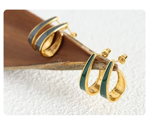 Close-up of gold-plated hammered metal hoop earrings with dark green enamel inlay