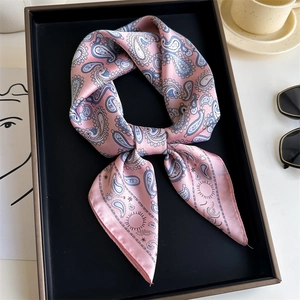 Pink paisley silk scarf tied in a bow on a black tray with stylish fashion accessories