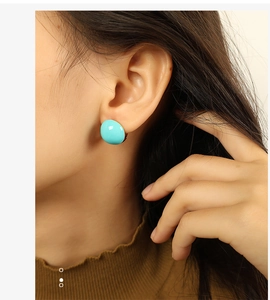 Close-up of model wearing round turquoise blue earrings in polished gold plated finish