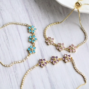 Bracciali regolabili in oro con fiori colorati e cristalli luccicanti su fondo legno
