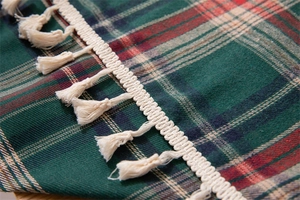 Macro shot of red and green plaid fabric with off-white fringe detail for Christmas decor