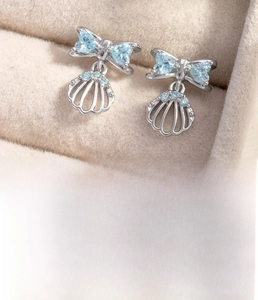 Macro detail of silver bow shell cartilage stud earrings with light blue zircons