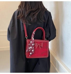 Detail of red bridal handbag featuring textured lace surface, bow accent, and silk scarf handle